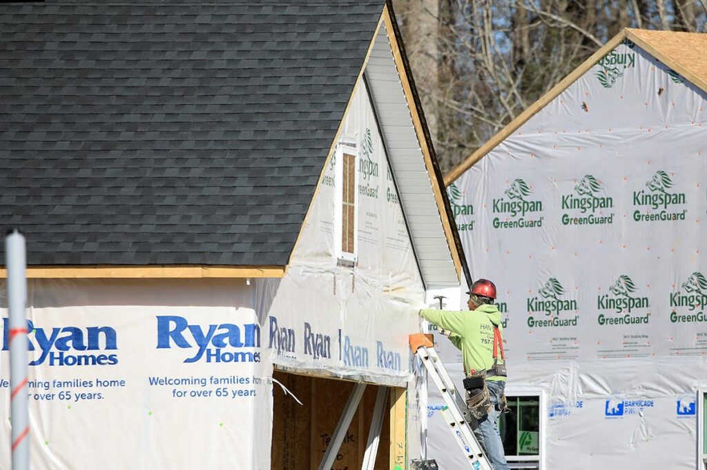 A construction worker hammers on the side of a house being built